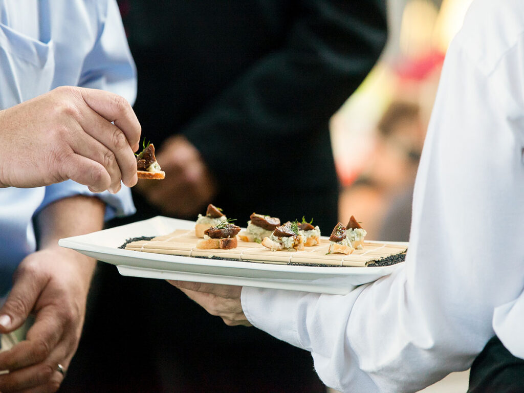 A server holding a tray full of snacks during a catered event