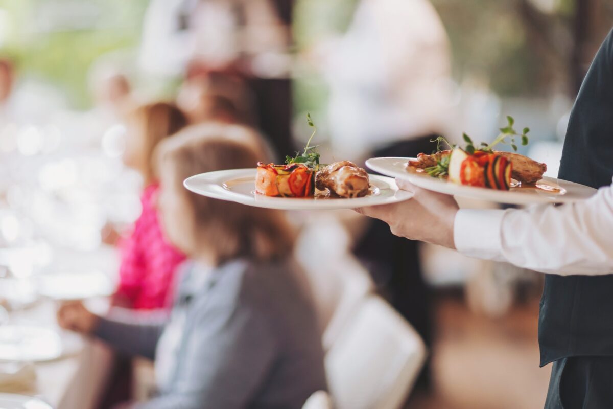 partial view of caterers in uniform holding plates of food